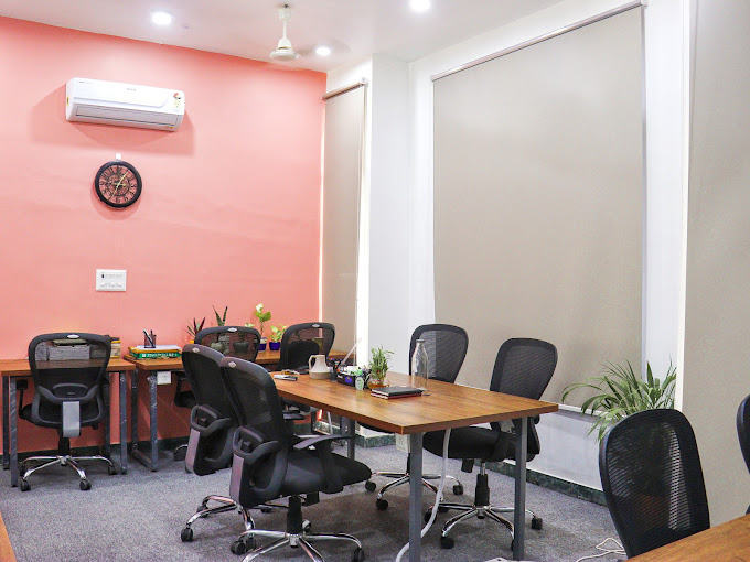 A cozy cabin interior with a wooden table, several chairs, a wall clock, air conditioning, and a decorative wall design at RAW Coworking space in Jaipur