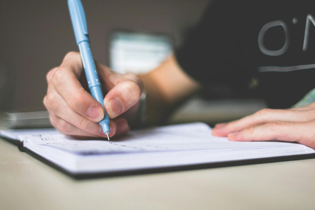 Person holding a pen and writing in a notebook for GST registration.