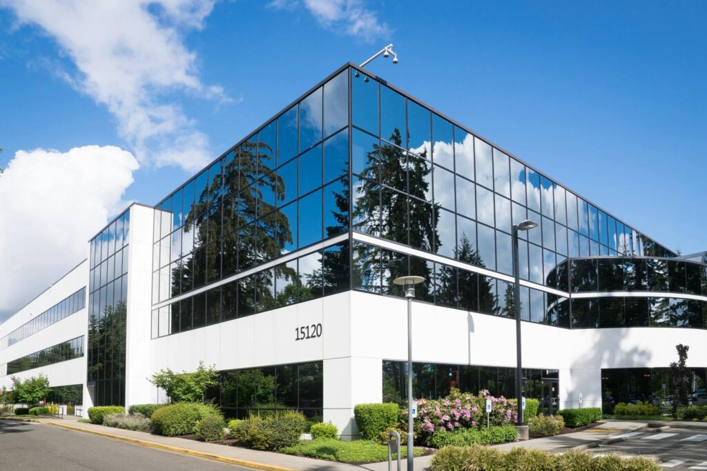 Modern white building with glass windows, surrounded by a green grass lawn, trees, and a road, representing a virtual office for GST registration.